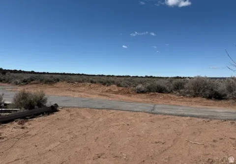 Expansive undeveloped land featuring a clear blue sky, distant natural brush, and a partial paved road
