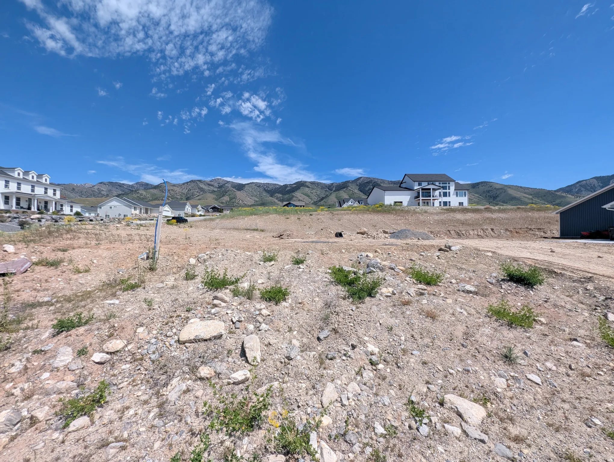 Expansive lot with mountain backdrop, surrounded by residential properties and a clear blue sky