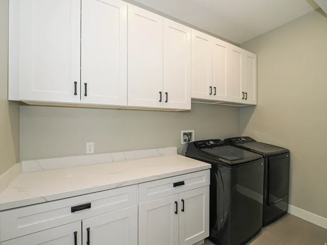 Laundry room featuring white shaker cabinetry with black hardware, white countertop surfaces, and neutral wall paint
