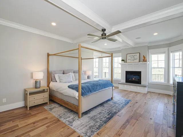 Spacious room featuring wood-finish flooring, a coffered ceiling with recessed lighting, a ceiling fan, and a fireplace with a white mantel and hearth
