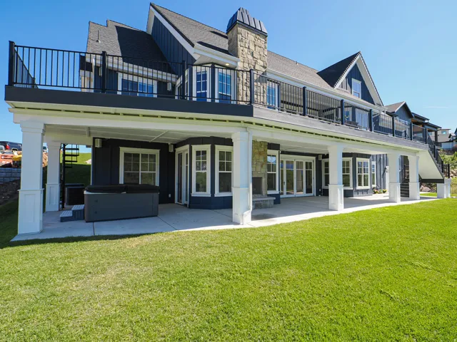 Expansive backyard featuring a covered patio, manicured lawn, and a spa area