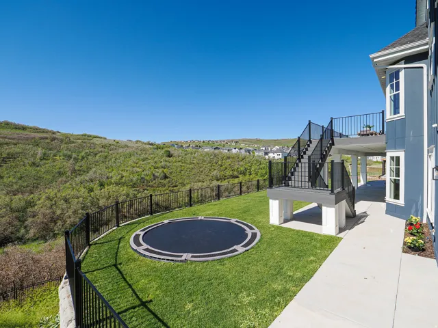 Expansive backyard featuring a built-in circular trampoline, manicured lawn, and black metal fencing