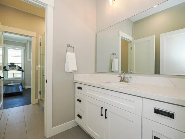Spacious bathroom featuring a white vanity with panel cabinetry and matte black hardware, a large vanity mirror, a white undermount sink, and light-toned tile flooring