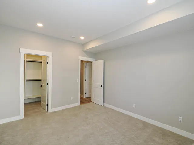 Carpeted room featuring recessed lighting, a built-in closet with shelving, white trim, and a second doorway revealing wood-finish flooring
