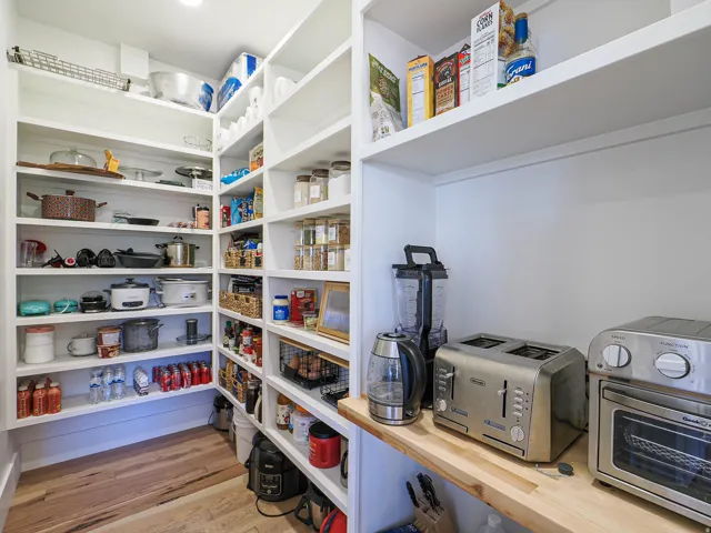 Walk-in pantry featuring extensive built-in shelving, durable wood-finish flooring, recessed lighting, and a dedicated countertop workspace