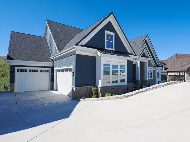 Contemporary home exterior featuring blue horizontal siding, stone veneer accents, multiple gable roofs with dark shingles, white trim, and a two-car garage with panel doors