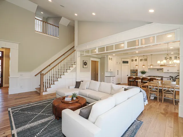 Open-concept living space featuring high ceilings, wood-finish flooring, a white staircase with wood handrails, and recessed lighting