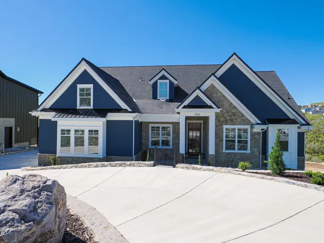 Contemporary home with blue siding, stone facade accents, white trim, a dark asphalt shingle roof, and a concrete driveway