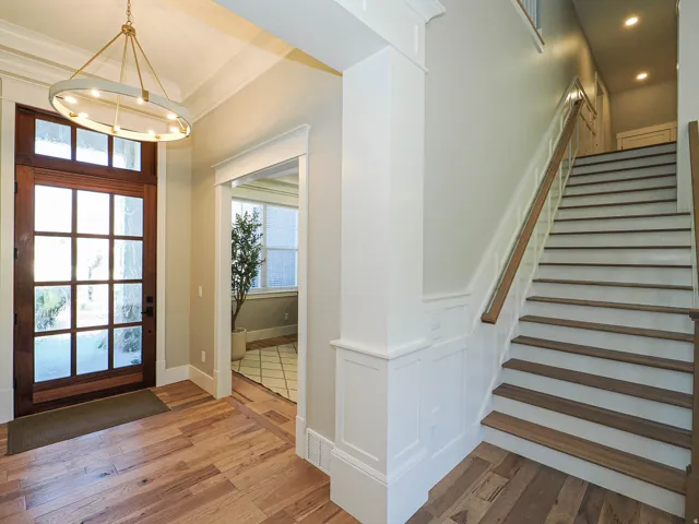 Entry foyer featuring a substantial wood-paneled front door, wood-finish flooring, a contemporary circular chandelier, and a staircase with wood treads and handrail