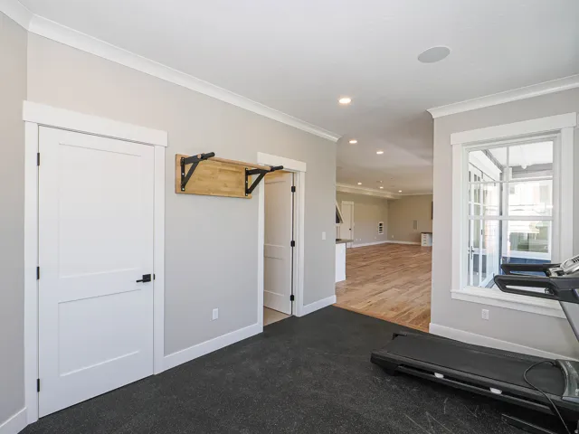 Dedicated fitness area featuring black rubber flooring, a built-in wooden workout shelf, and ample natural light from a large window