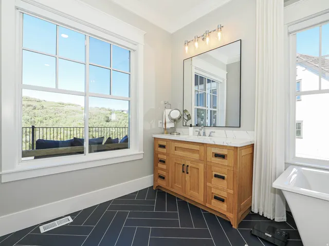 Bathroom featuring a freestanding tub, wood-finish vanity with a quartz countertop, rectangular mirror, and black herringbone-patterned floor tiles