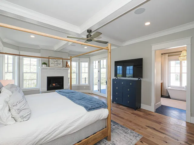 Spacious room featuring wood-finish flooring, a tray ceiling, and a fireplace with a white mantel