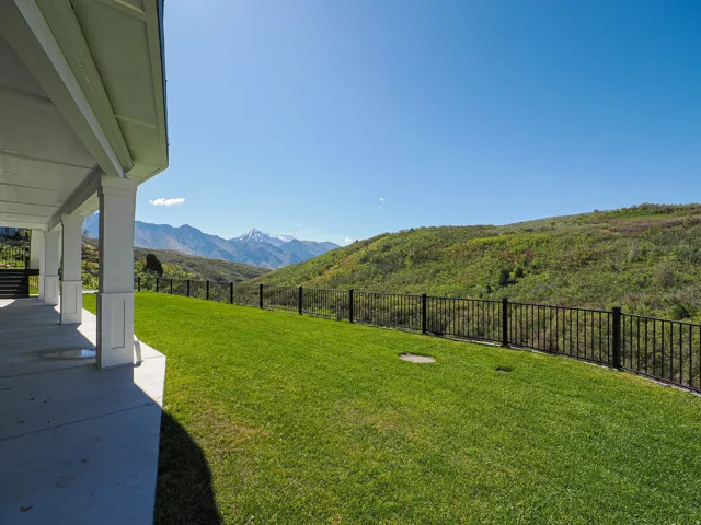 Expansive green lawn bordered by a black metal fence, offering mountain scenery