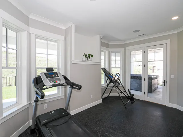 Dedicated fitness space featuring bay windows, durable rubber flooring, white trim, and direct patio access through French doors