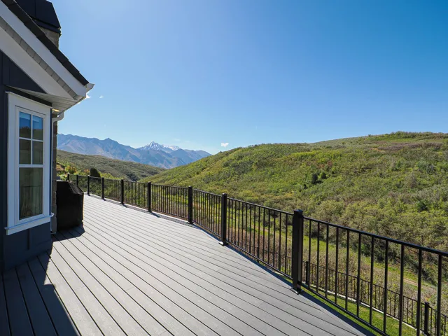 Expansive exterior deck featuring composite decking, black metal railings, and a snow-capped mountain backdrop
