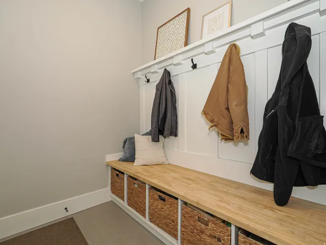 Built-in mudroom bench with natural wood-finish top, integrated storage cubbies, and vertical paneled wainscoting