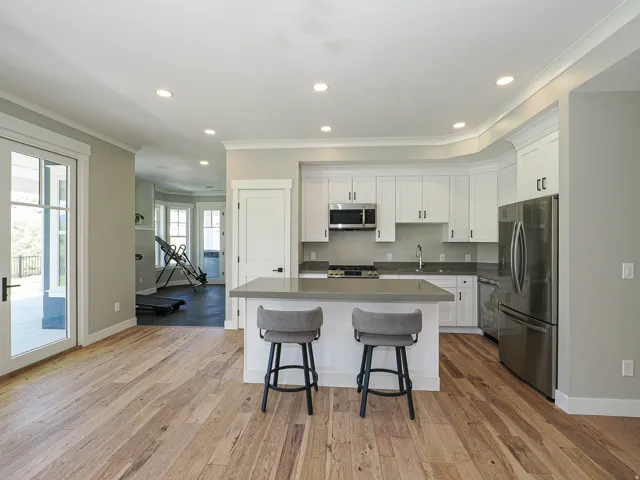 Open-concept kitchen featuring white cabinetry, stainless steel appliances, a center island with countertop seating, recessed lighting, and wood-finish flooring
