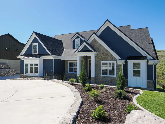 Contemporary home exterior featuring a dark blue facade, stone accents, white trim, a multi-gable roofline, and a curved concrete driveway