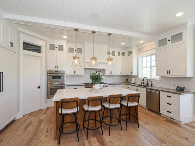 Gourmet kitchen featuring a substantial wood-finish island with seating, extensive white cabinetry with matte black hardware, integrated stainless steel appliances, wood-finish flooring, and shiplap ceiling details