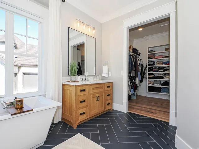Bathroom featuring a freestanding soaking tub, single vanity with wood-finish cabinetry and stone countertop, and herringbone-patterned floor tiling