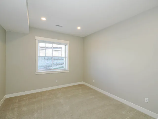 Carpeted room featuring a white-framed window with blinds, recessed ceiling lighting, and light-toned walls