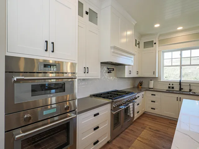 Gourmet kitchen featuring a stainless steel wall oven and microwave, a professional-grade gas range, custom white cabinetry, dark countertops, and wood-finish flooring
