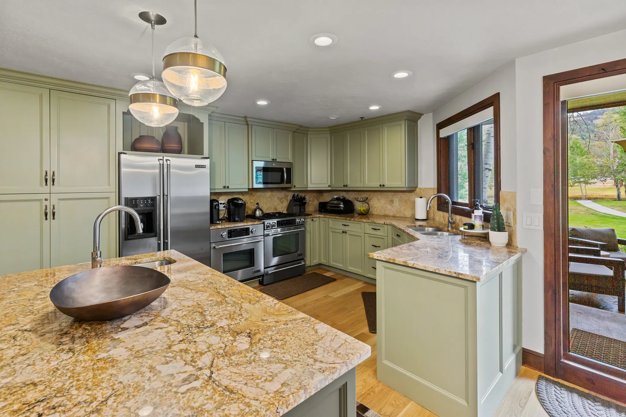 Kitchen featuring light green cabinetry, stainless steel appliances, granite countertops, wood-finish flooring, and pendant lighting