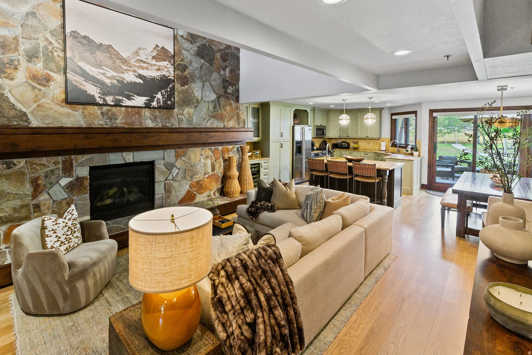 Open-concept living area featuring a stone fireplace with a substantial wood mantel, light wood-finish flooring, and recessed lighting