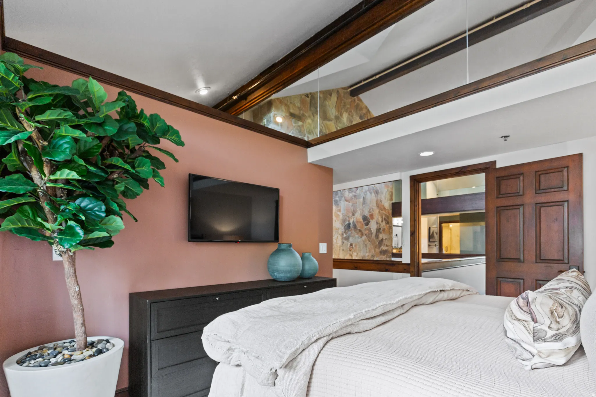 Bedroom featuring a high vaulted ceiling with exposed wood beams, a built-in wall-mounted television, and a paneled wood door