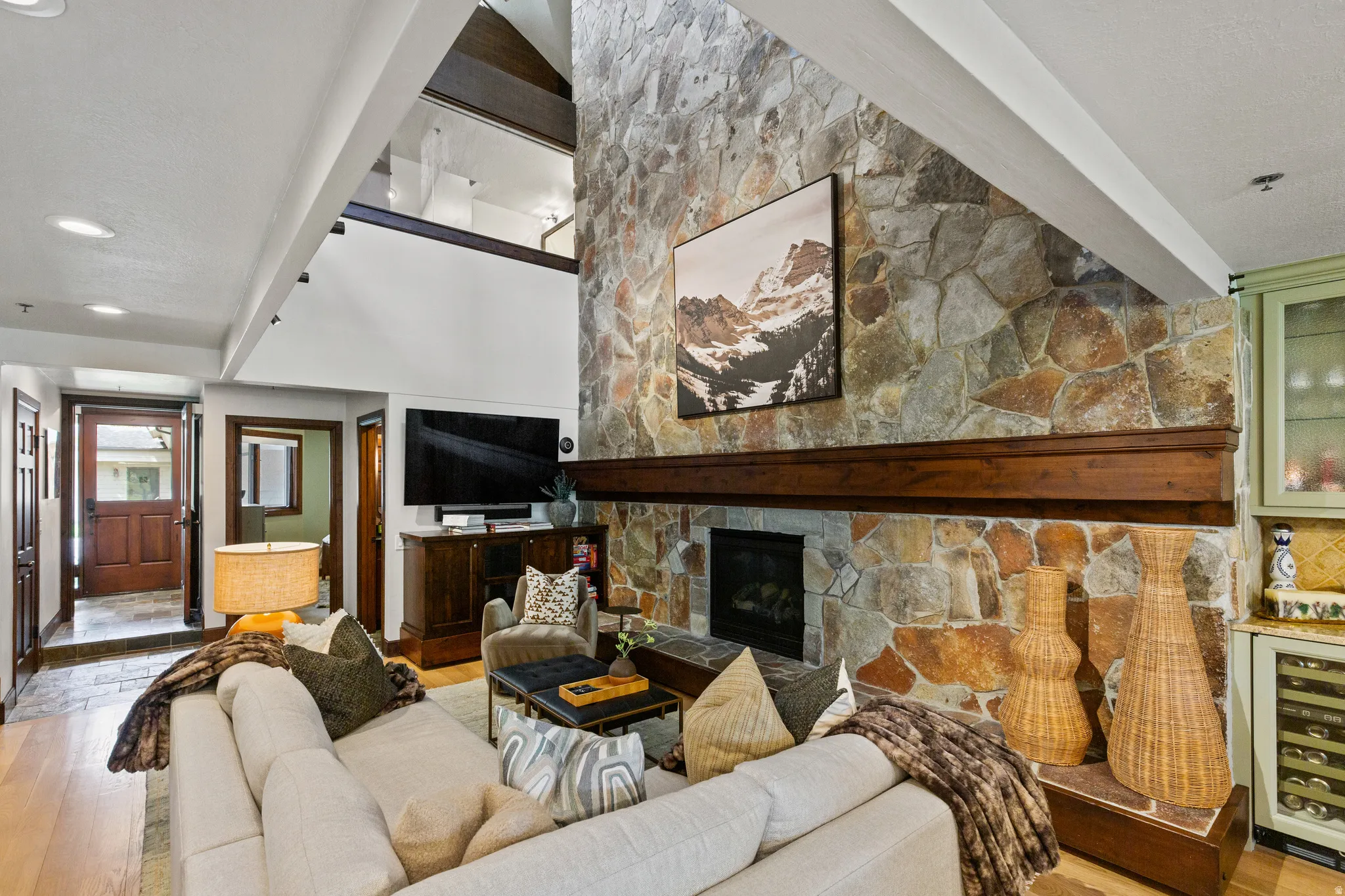 Soaring ceilings define this living space, featuring a floor-to-ceiling stone fireplace with a substantial wood mantel