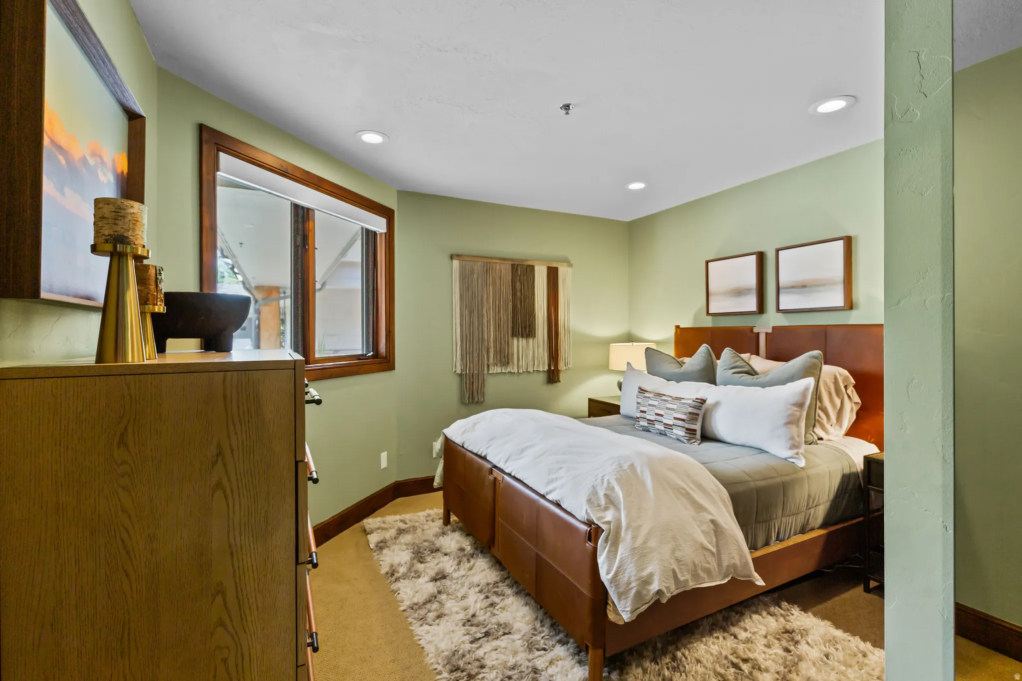 Recessed lighting illuminates a bedroom featuring a rich wood-frame window, light green walls, and coordinating wood trim