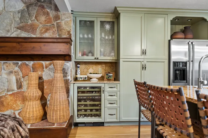 Built-in dry bar featuring a stone backsplash, integrated wine refrigerator, and light green cabinetry with frosted glass doors
