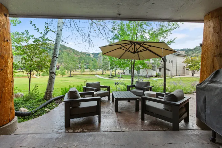 Covered patio featuring robust log columns, a concrete slab, and a green expanse beyond
