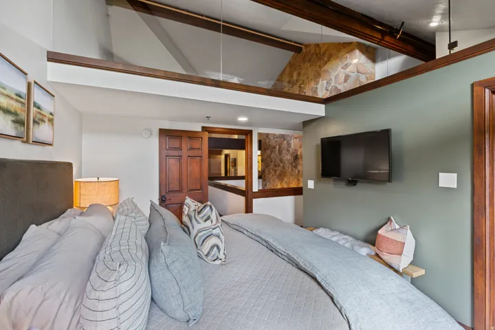Room featuring a high ceiling, exposed wood beams, and a stone accent wall