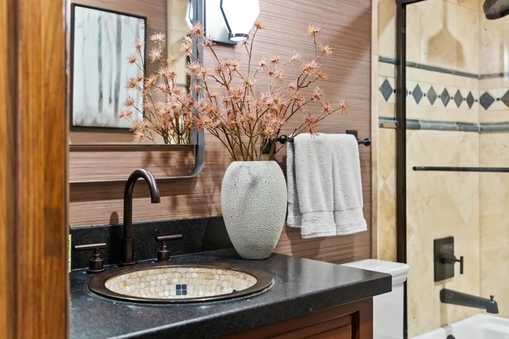 Vanity featuring a mosaic-tiled basin, dark stone countertop, and oil-rubbed bronze fixtures