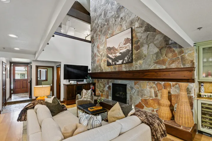 Soaring ceilings define this living space, featuring a floor-to-ceiling stone fireplace with a substantial wood mantel