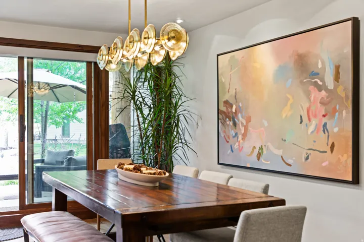 Dining area featuring a wood-finish table, a modern linear chandelier with gold-tone accents, and a large abstract art piece