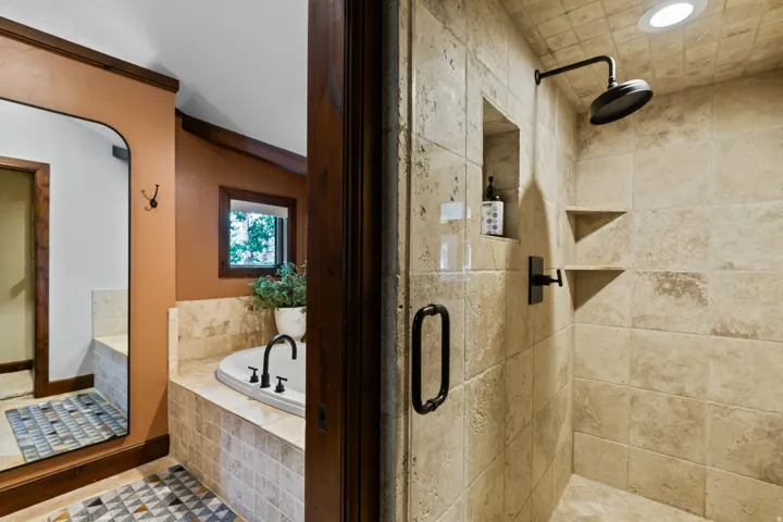 Walk-in shower with natural stone tile, recessed niche, and matte black fixtures