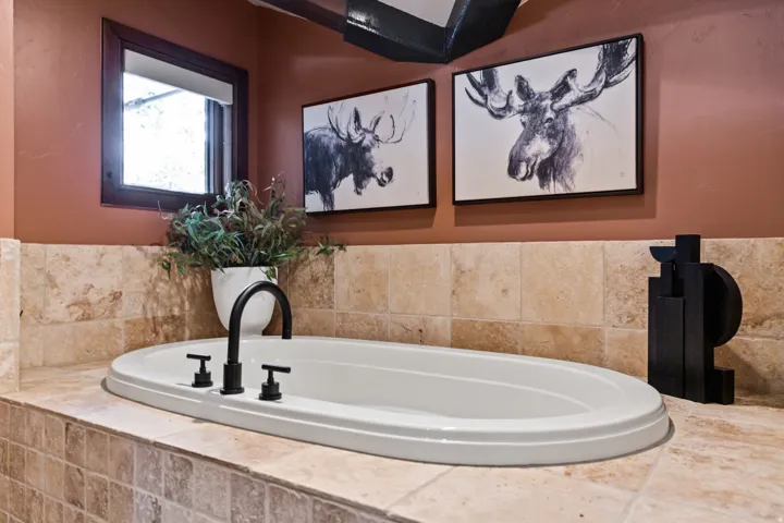 Built-in soaking tub with matte black fixtures, set within a travertine tile surround