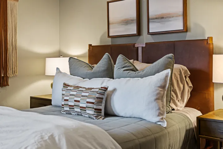 Bedroom featuring a leather-paneled headboard, recessed wall art, and matching bedside tables with lamps