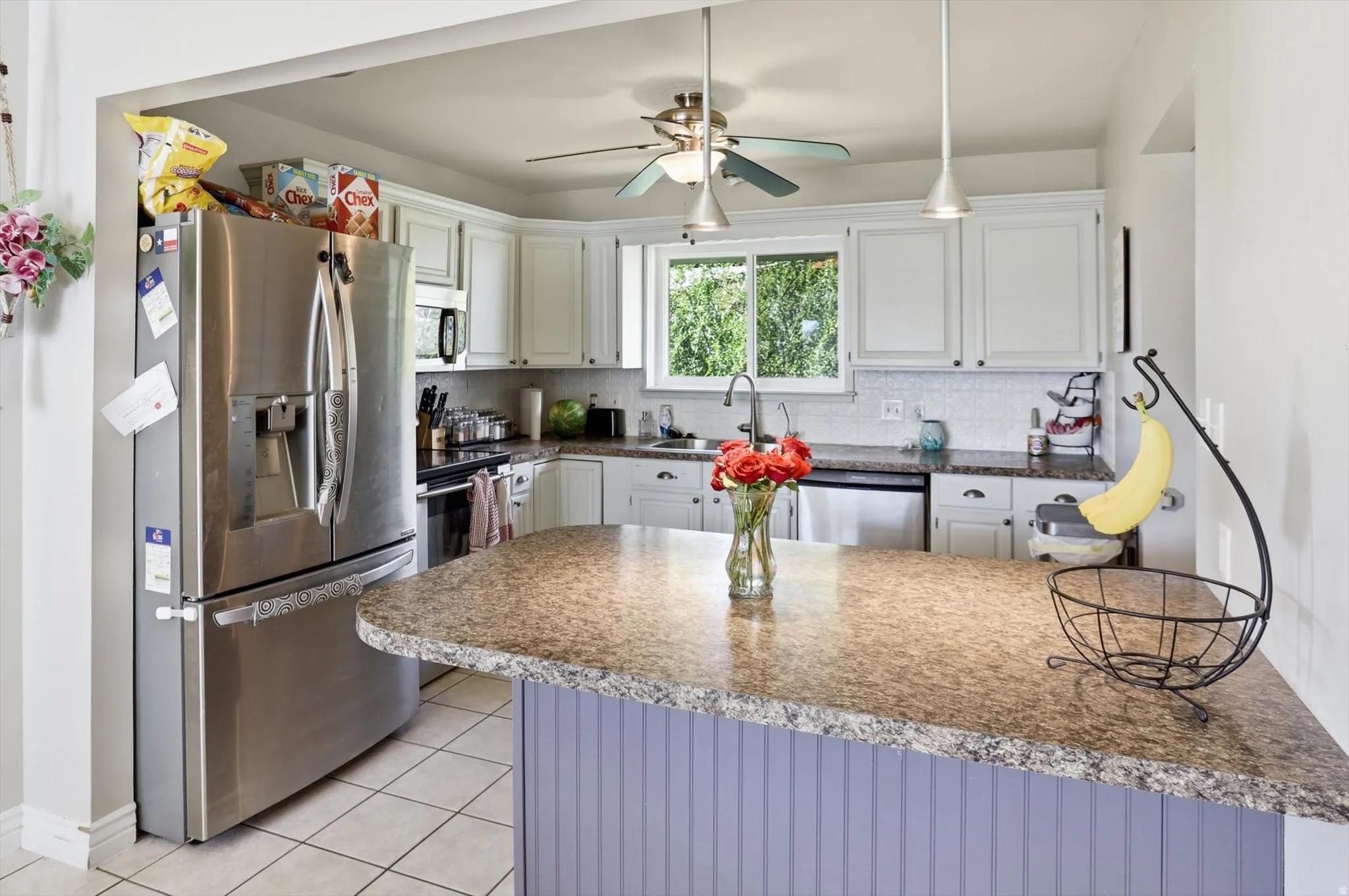 Kitchen featuring a central island with a speckled countertop, white cabinetry, stainless steel appliances, tile flooring, and a window above the sink