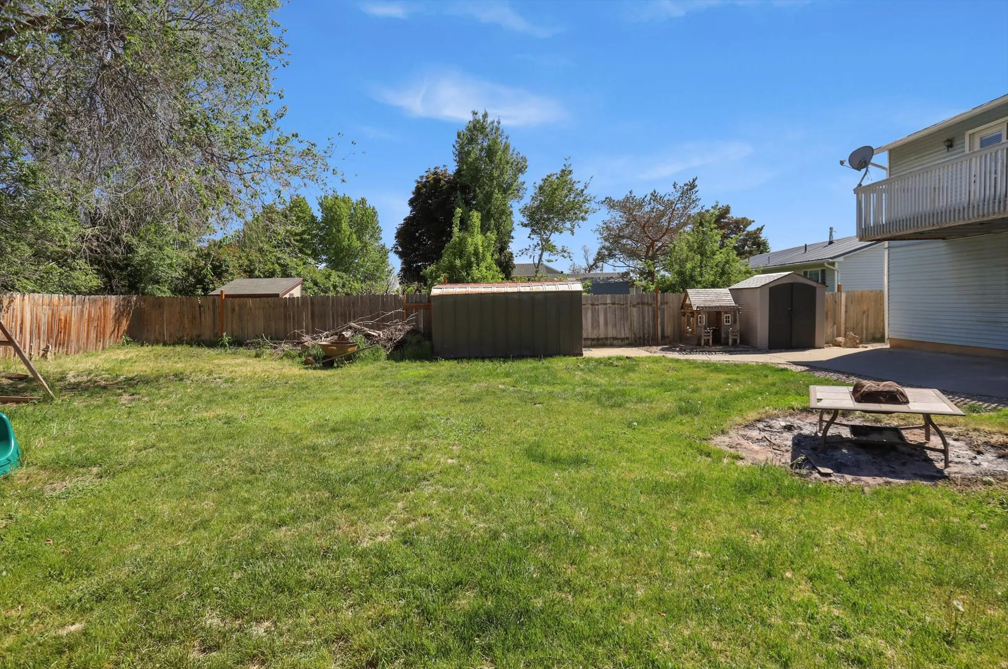 Expansive backyard featuring a manicured lawn, full wood fencing, and multiple storage sheds
