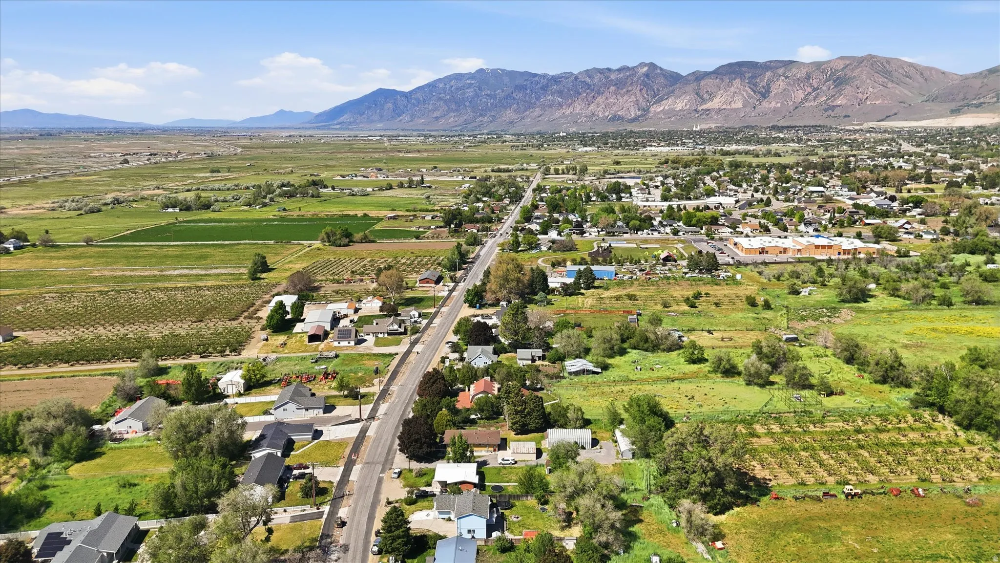 Aerial perspective showcasing a residential area with a prominent roadway, surrounded by green fields and distant mountains