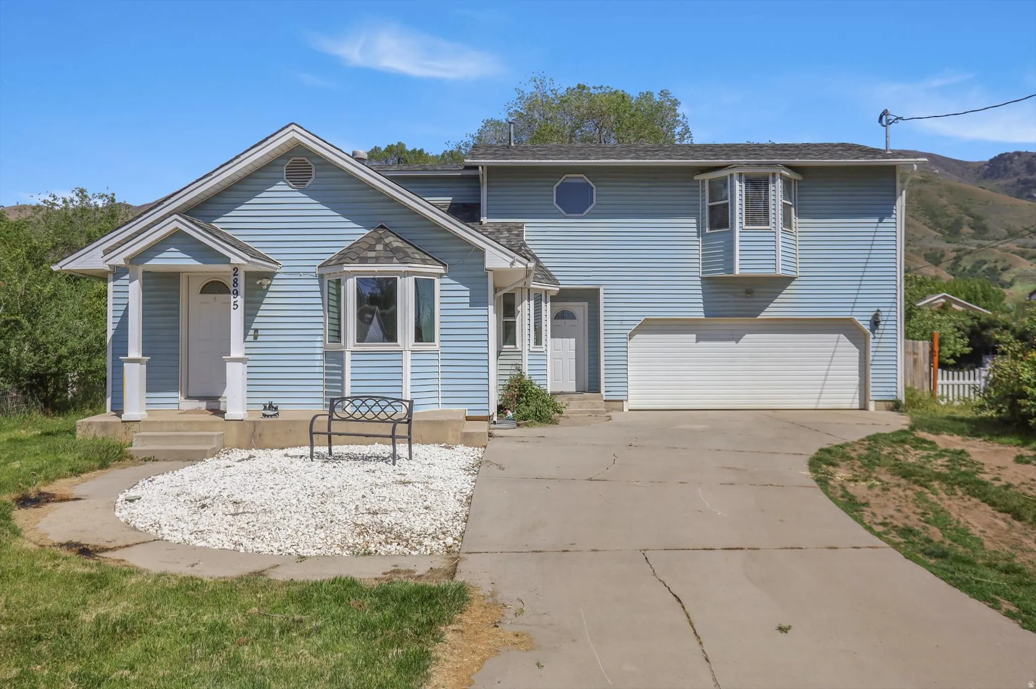 Light blue siding exterior featuring a two-car garage, a covered front porch, a bay window, and a dedicated driveway