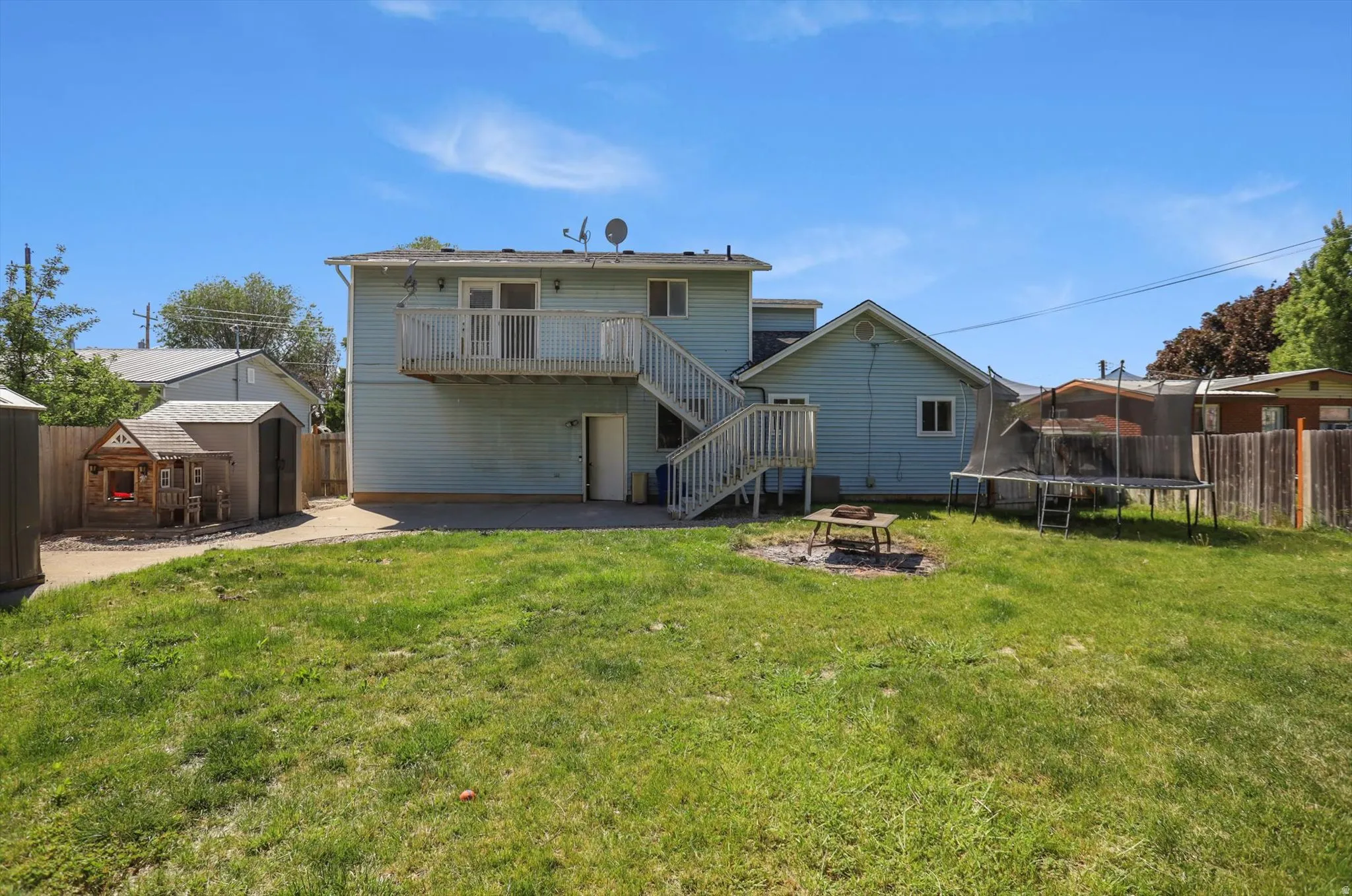 Expansive backyard featuring a manicured lawn, a large concrete patio, and a tiered deck with outdoor stairs