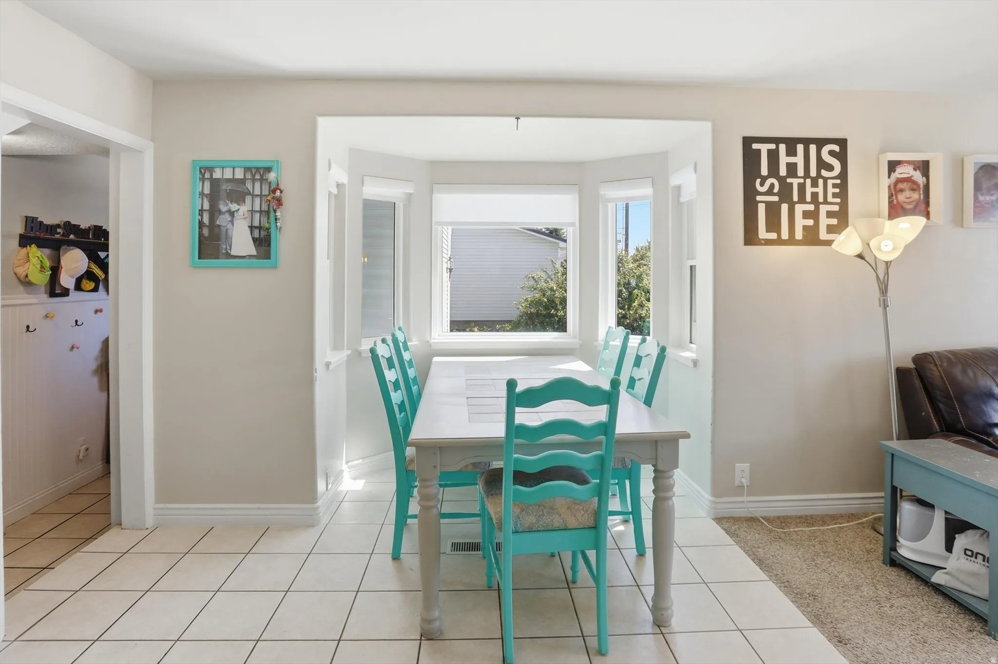 Bright dining area featuring a bay window, neutral wall paint, white trim, and square tile flooring