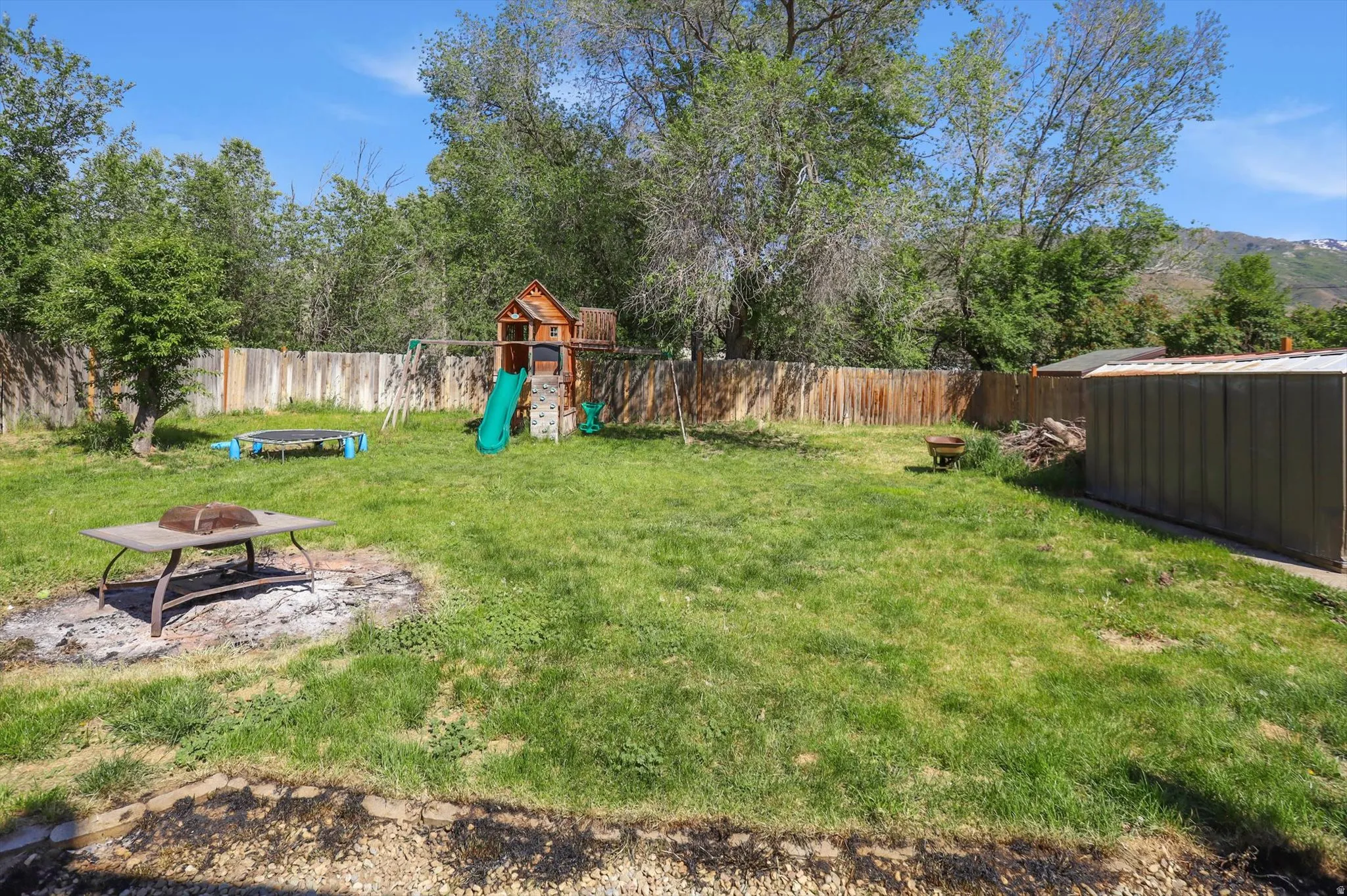 Expansive fenced backyard featuring a grassy lawn, mature trees, and a storage shed