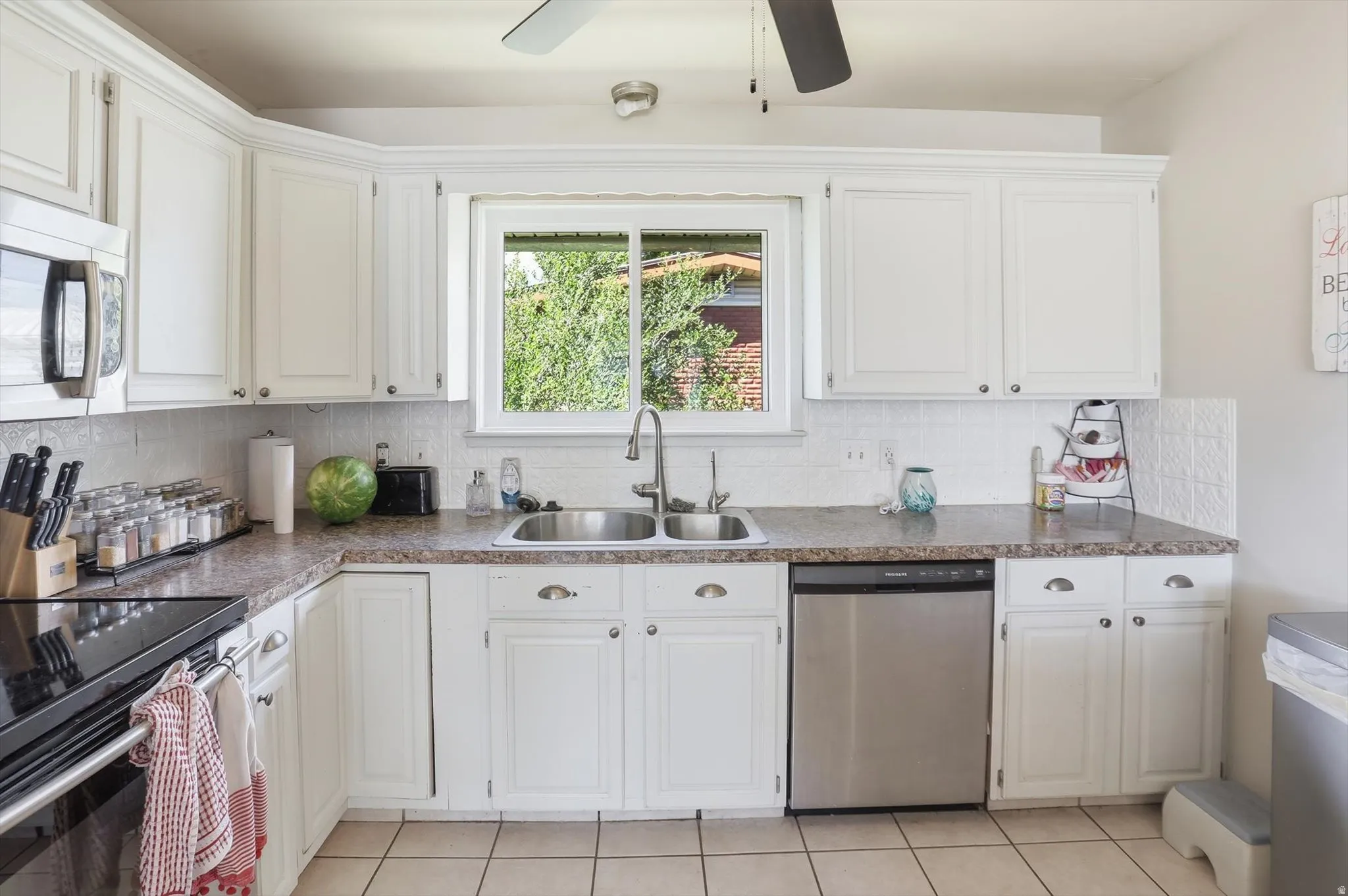 Kitchen featuring white cabinetry, a double basin stainless steel sink, a stainless steel dishwasher, a built-in microwave, and tile flooring