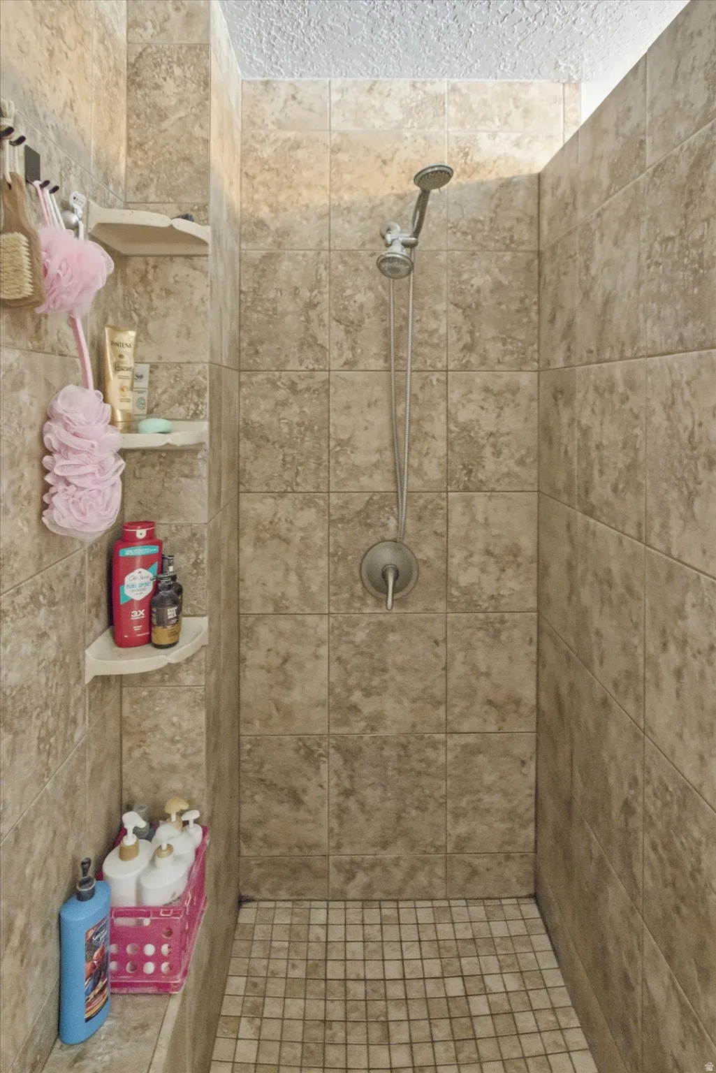 Walk-in shower with full-height large format wall tiling, handheld shower fixture, built-in corner shelving, and mosaic tile flooring