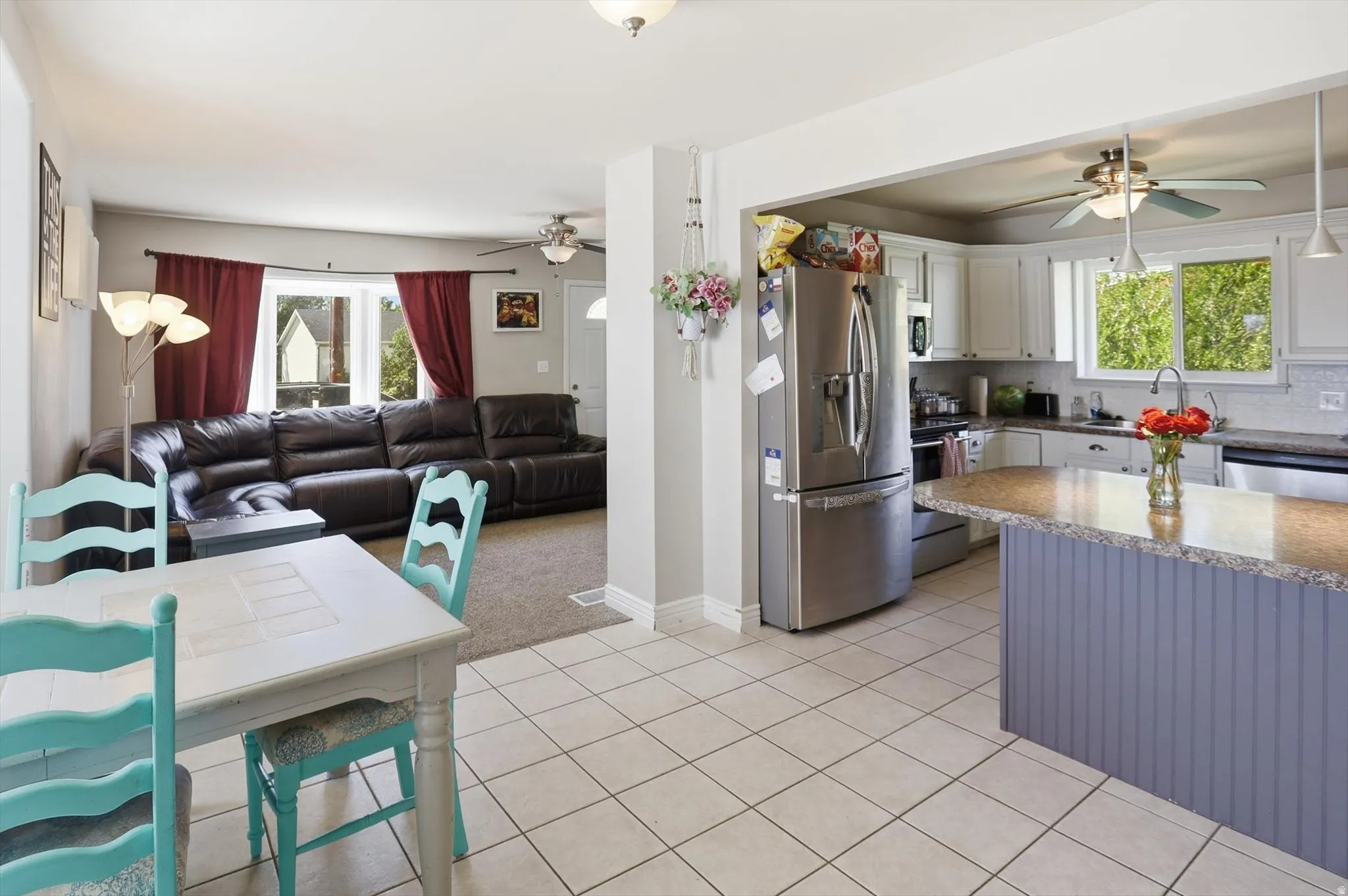 Open-concept kitchen and dining area featuring tile flooring, white cabinetry, a built-in kitchen island with a stone-finish countertop, and stainless steel appliances